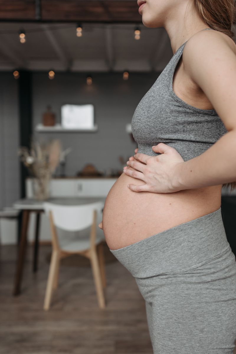 Close-up of an expectant mother cradling her belly in warm sunlight
