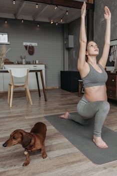 Pregnant woman doing yoga indoors with dachshund dog nearby, embodying healthy lifestyle.