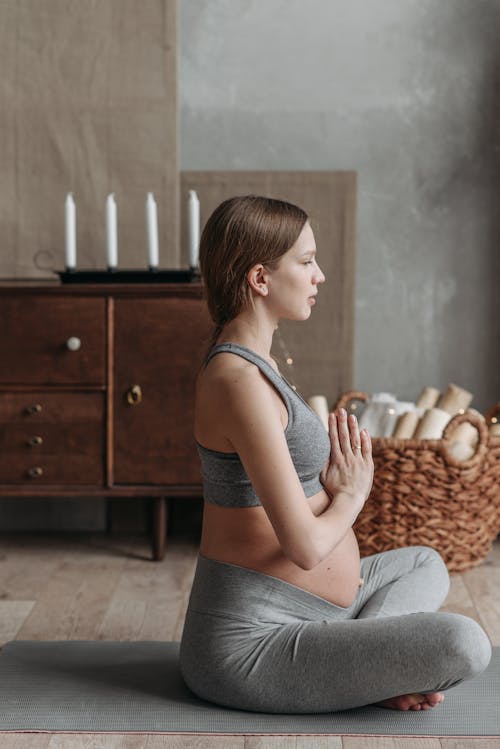 Free Woman in Gray Tank Top and Gray Pants Sitting on Brown Wooden Bed Stock Photo