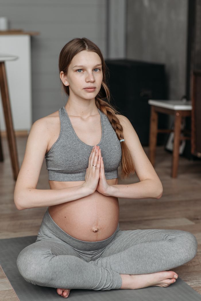 Woman in grey maternity leggings seated on a mat. Photo by Pavel Danilyuk on Pexels