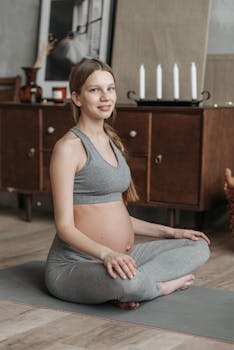 Pregnant woman sitting in yoga pose on mat at home. Perfect for health and wellness themes.