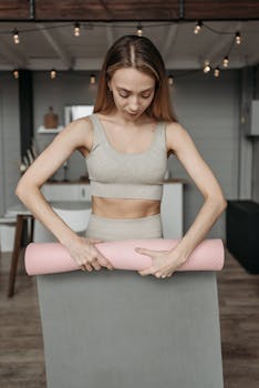 Young woman rolling up her yoga mat indoors, ready to start her fitness routine.