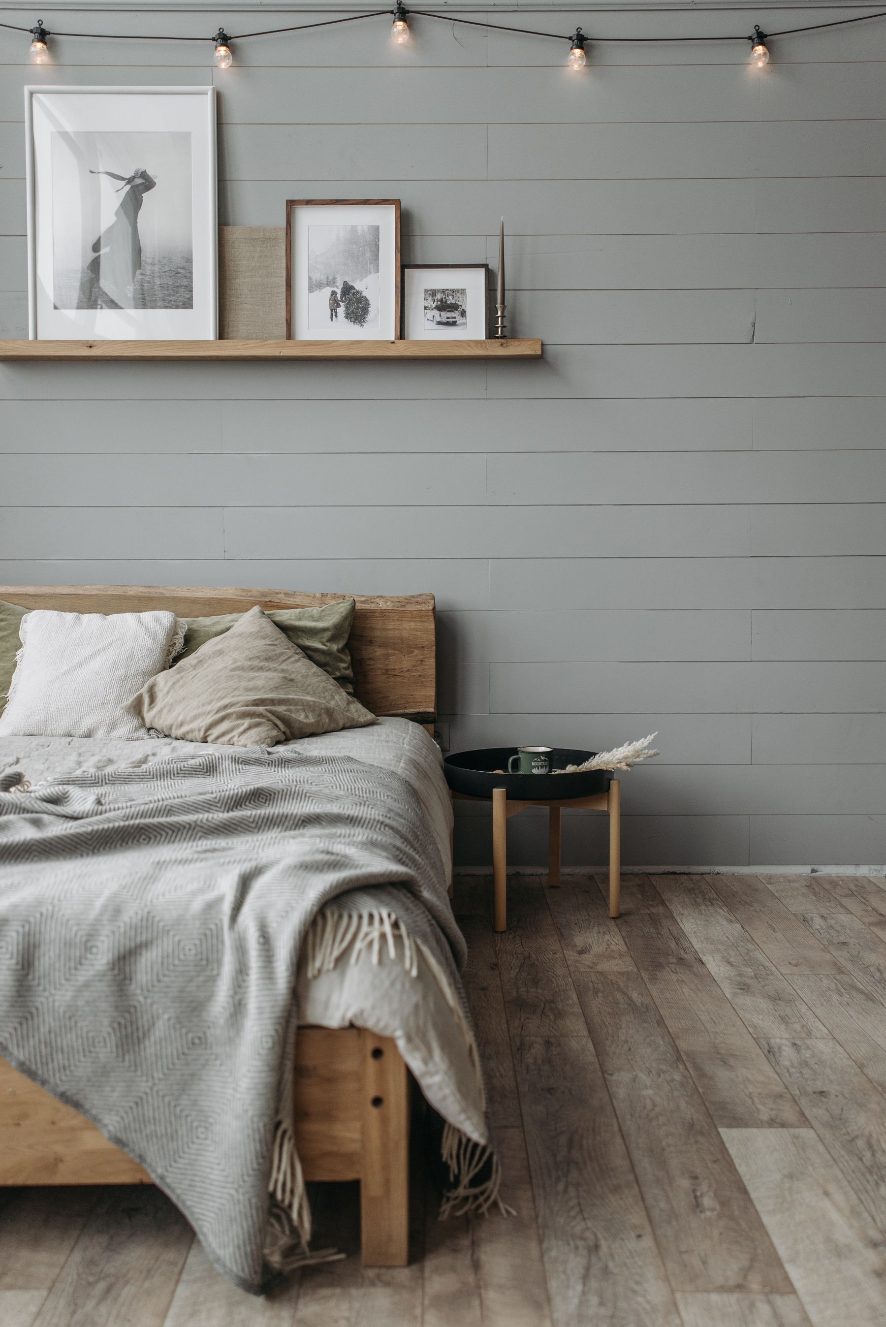 Warm wood bed with a low headboard, neutral linen, gray blanket and a small round side table
