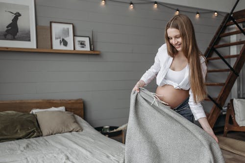 Free Pregnant Woman in White Crop Top Making Bed Stock Photo