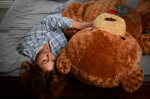 Serene woman lying on bed with big plush bear