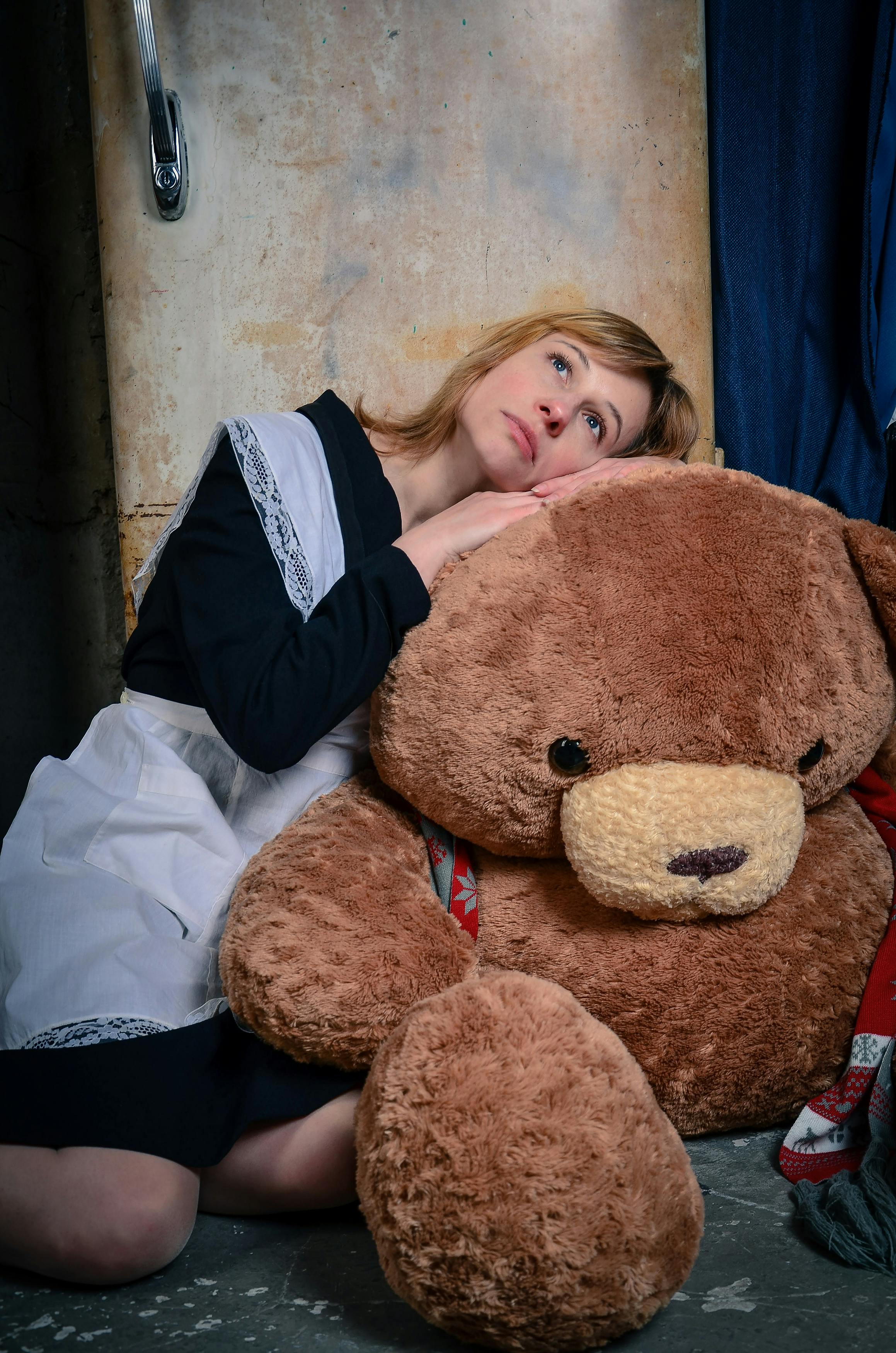 Free Thoughtful woman in uniform leaning on large teddy bear indoors, conveying emotion. Stock Photo