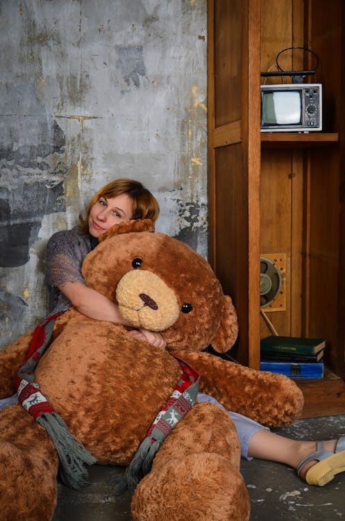 Positive woman hugging big teddy bear on floor Free Stock Photo