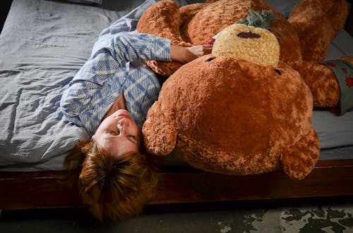 Relaxed woman lying on bed with big plush bear