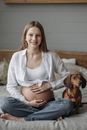 A Woman With Hands on Belly Sitting on Bed with a Brown Dog