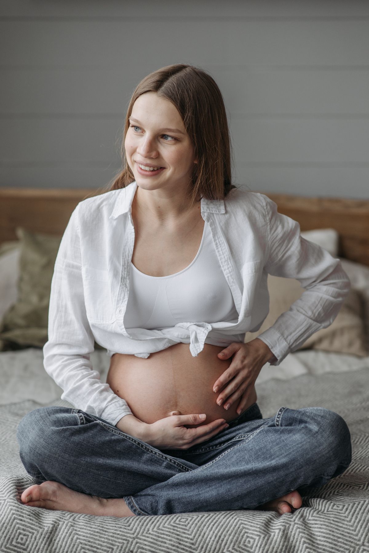 Smiling pregnant woman sitting comfortably on a bed