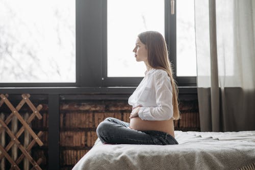 Free 
A Pregnant Woman Holding Her Baby Bump while Sitting on a Bed Stock Photo