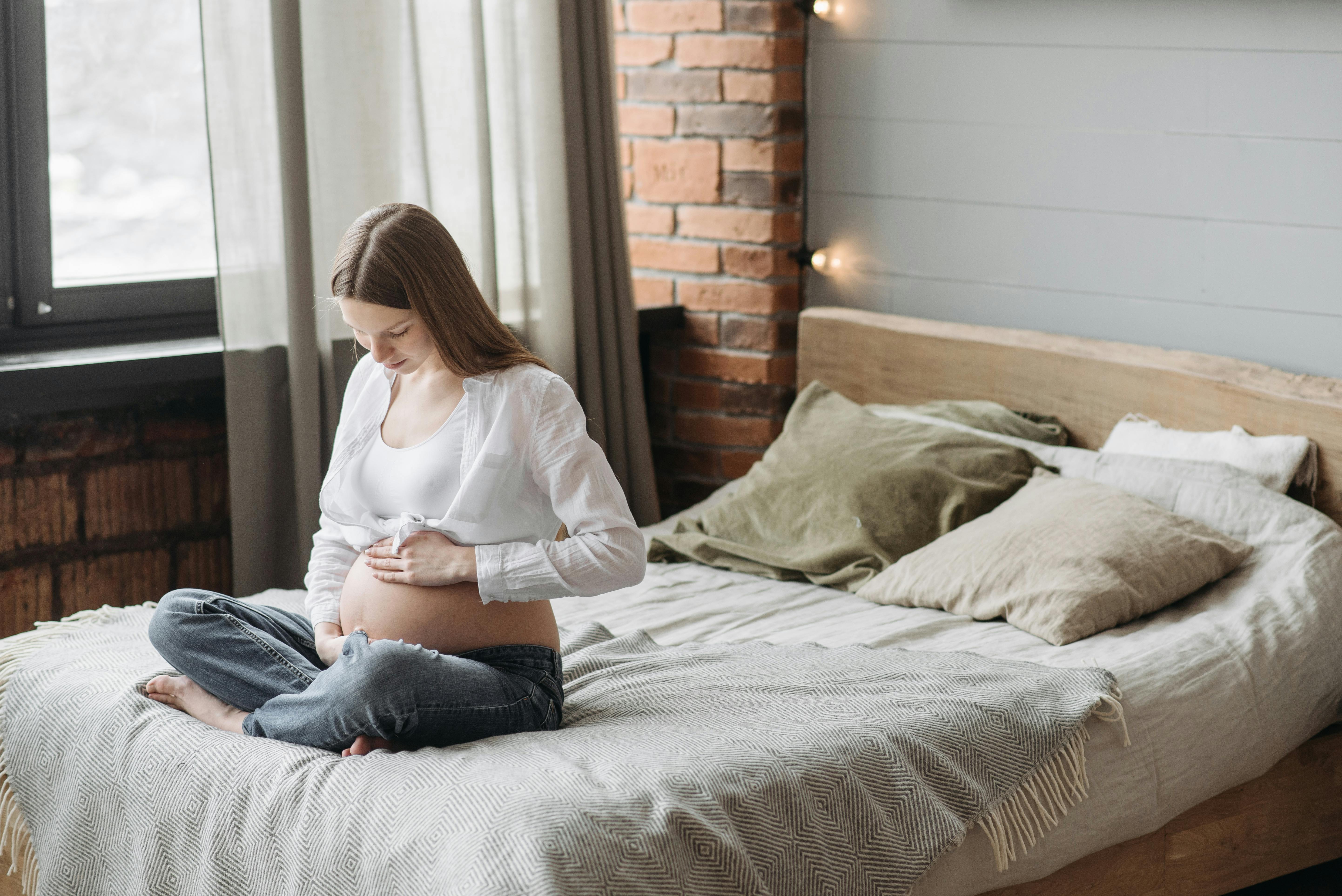 pregnant woman sitting on bed holding her belly