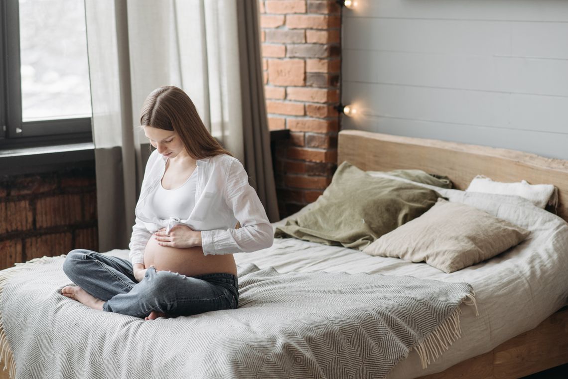 Expectant mother sitting comfortably on a bed and holding her baby bump