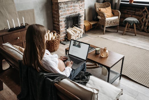 Pregnant woman working remotely from home, sitting on a couch with a laptop, cozy interior.