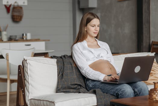 Expectant mother sitting on sofa using laptop in a cozy living room setting.