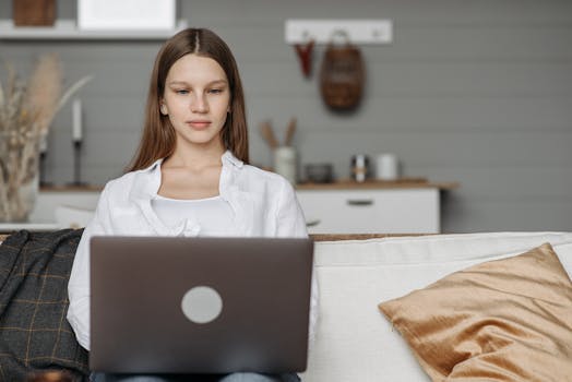 Young woman in a cozy home setting focused on her laptop, embodying modern remote work.