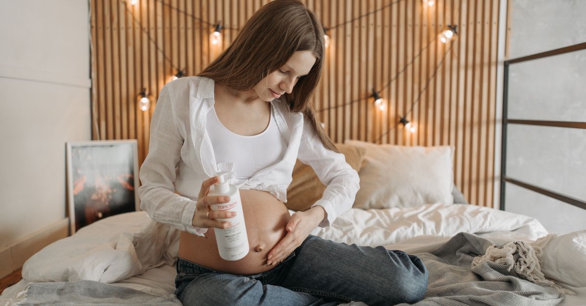 ベッドでおなかにクリームをなじませる妊娠中の女性のイメージ