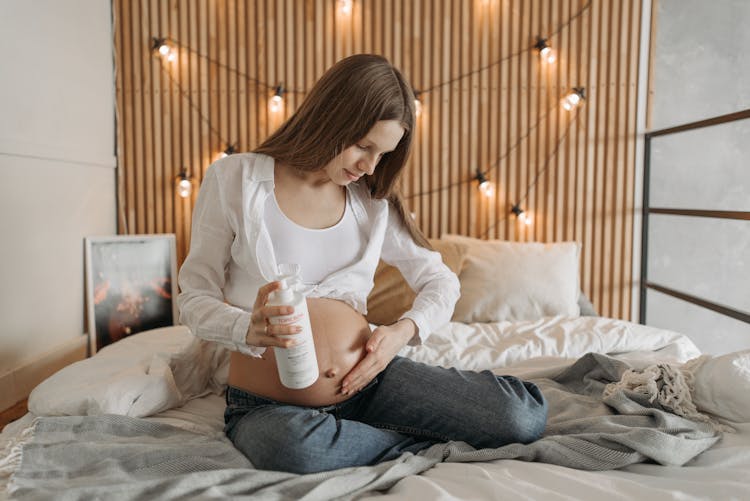 A Pregnant Woman Rubbing Lotion On Her Belly