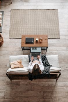 A woman using a laptop on a couch in a cozy home setting, perfect for remote work themes.