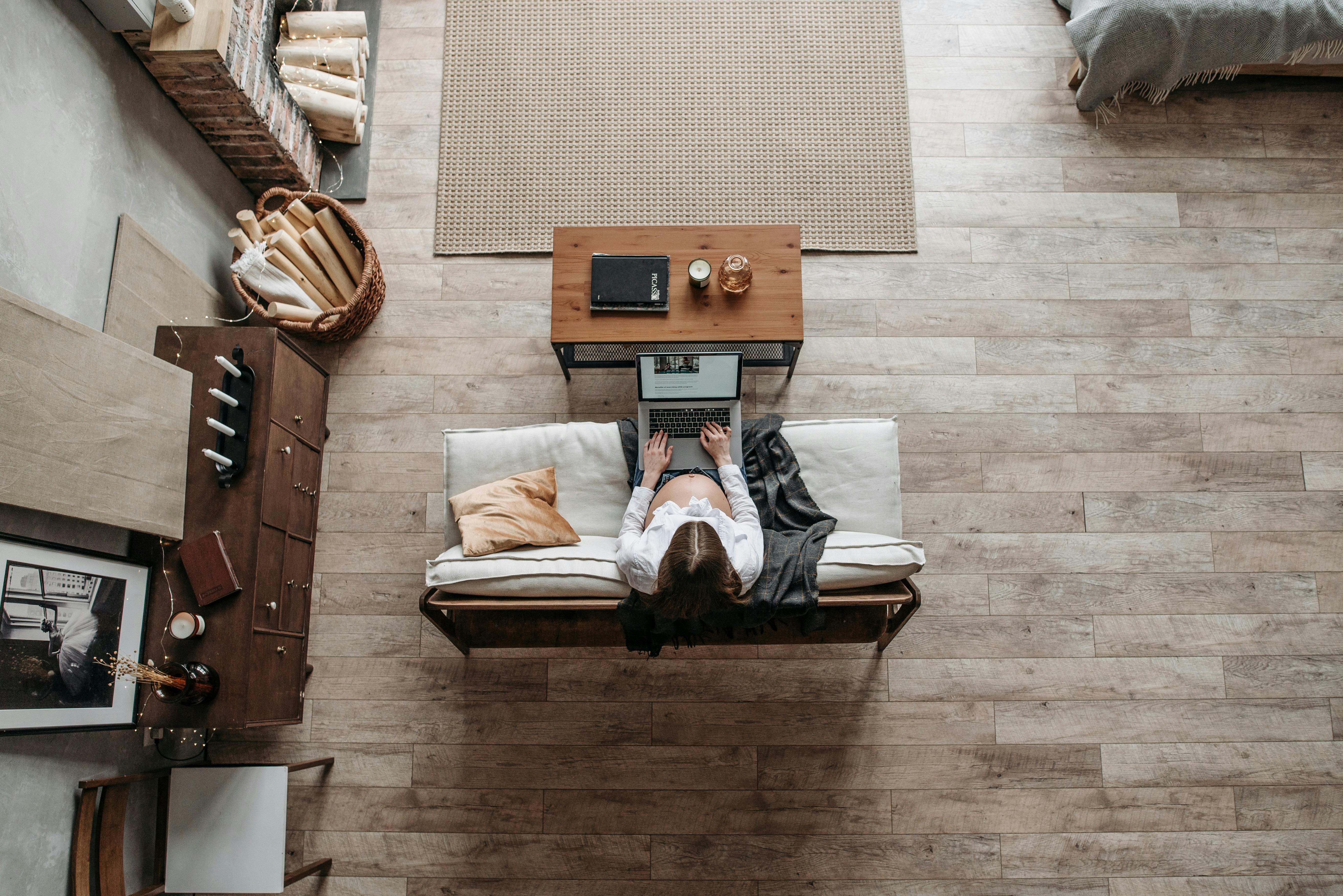 Pregnant woman working from home in a cozy living room environment with a laptop on a wooden floor.