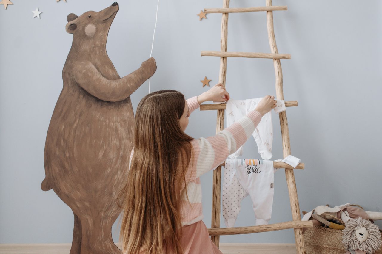woman organizes baby clothes on wooden ladder in decorated nursery coz