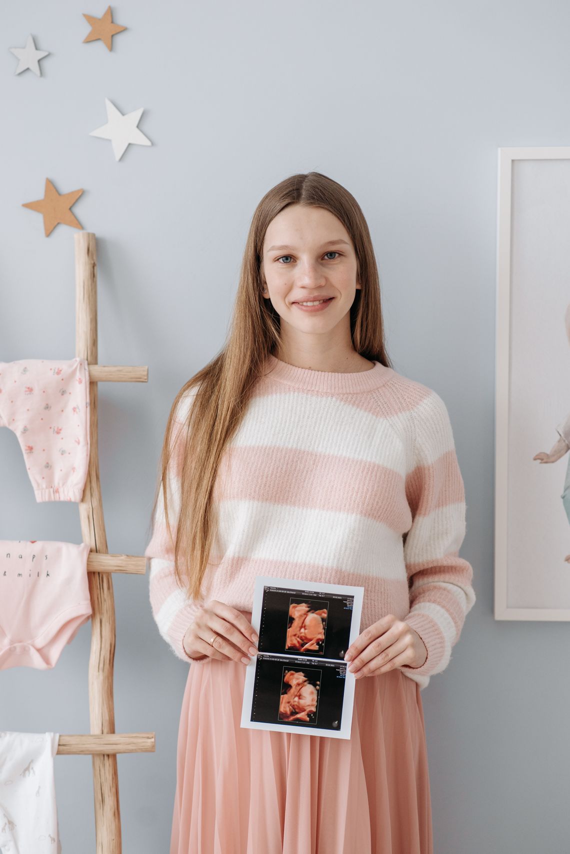 Smiling pregnant woman holding ultrasound pictures in a nursery with her face clearly visible