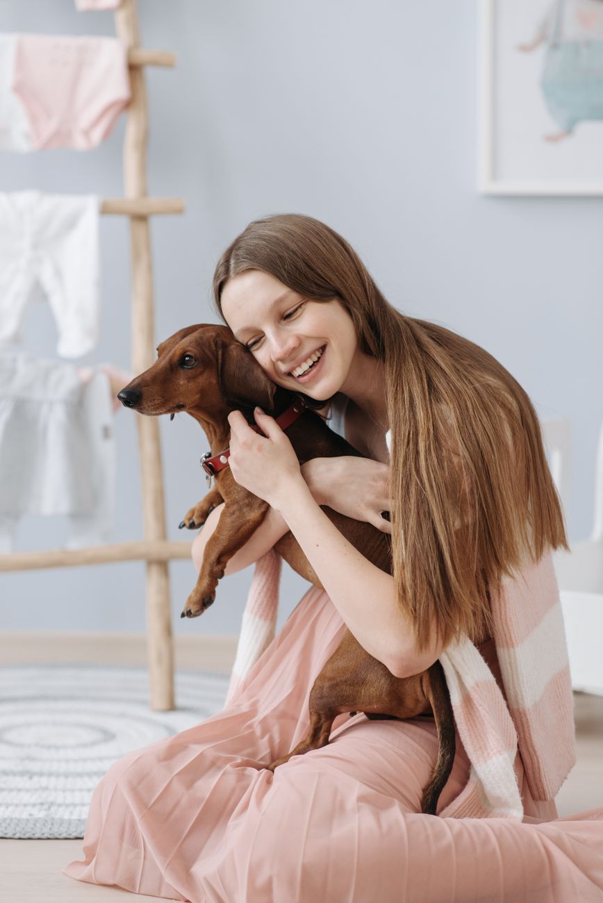 Smiling woman embracing her dachshund dog in a cozy indoor setting. Happy pet care moment.