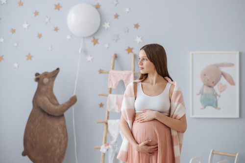 Free A beautiful pregnant woman in a stylish baby room, holding her belly. Stock Photo