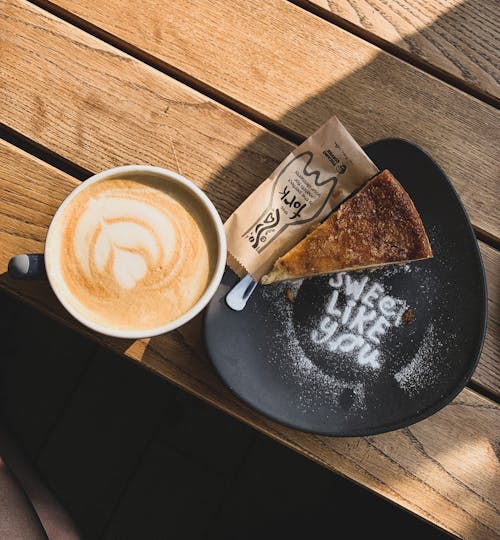 Top view of tasty coffee with latte art on foam near piece of dessert with Sweet Like You inscription in cafeteria