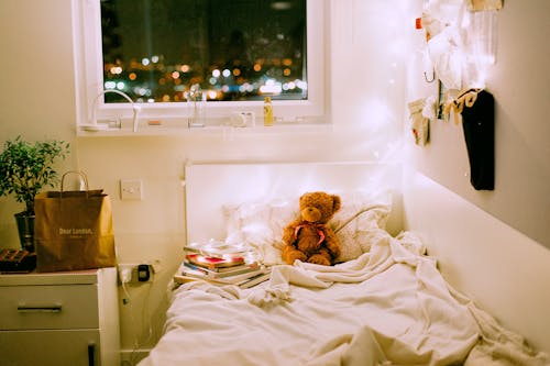 Bezpłatne Niedźwiedź Brunatny Pluszowa Na Kołdrę W Białym łóżku Wewnątrz Oświetlonej Sypialni Zdjęcie z galerii