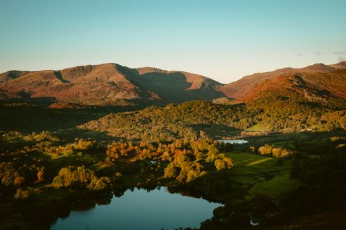 Free Stunning aerial view of a lake surrounded by forests and mountains in vibrant daylight. Stock Photo