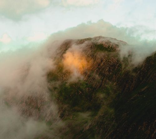 Free Aerial view of a misty mountain peak with golden light diffusing through clouds at dawn. Stock Photo