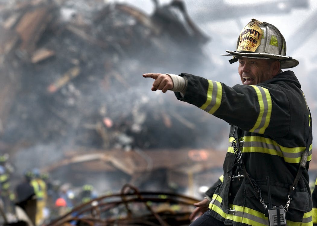 Gratis Pemadam Kebakaran Mengenakan Seragam Hitam Kuning Menunjuk Sesuatu Foto Stok