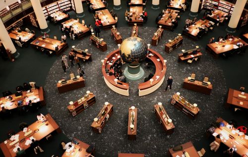 Free Busy library interior with a large globe centerpiece and people working at wooden tables. High angle view. Stock Photo
