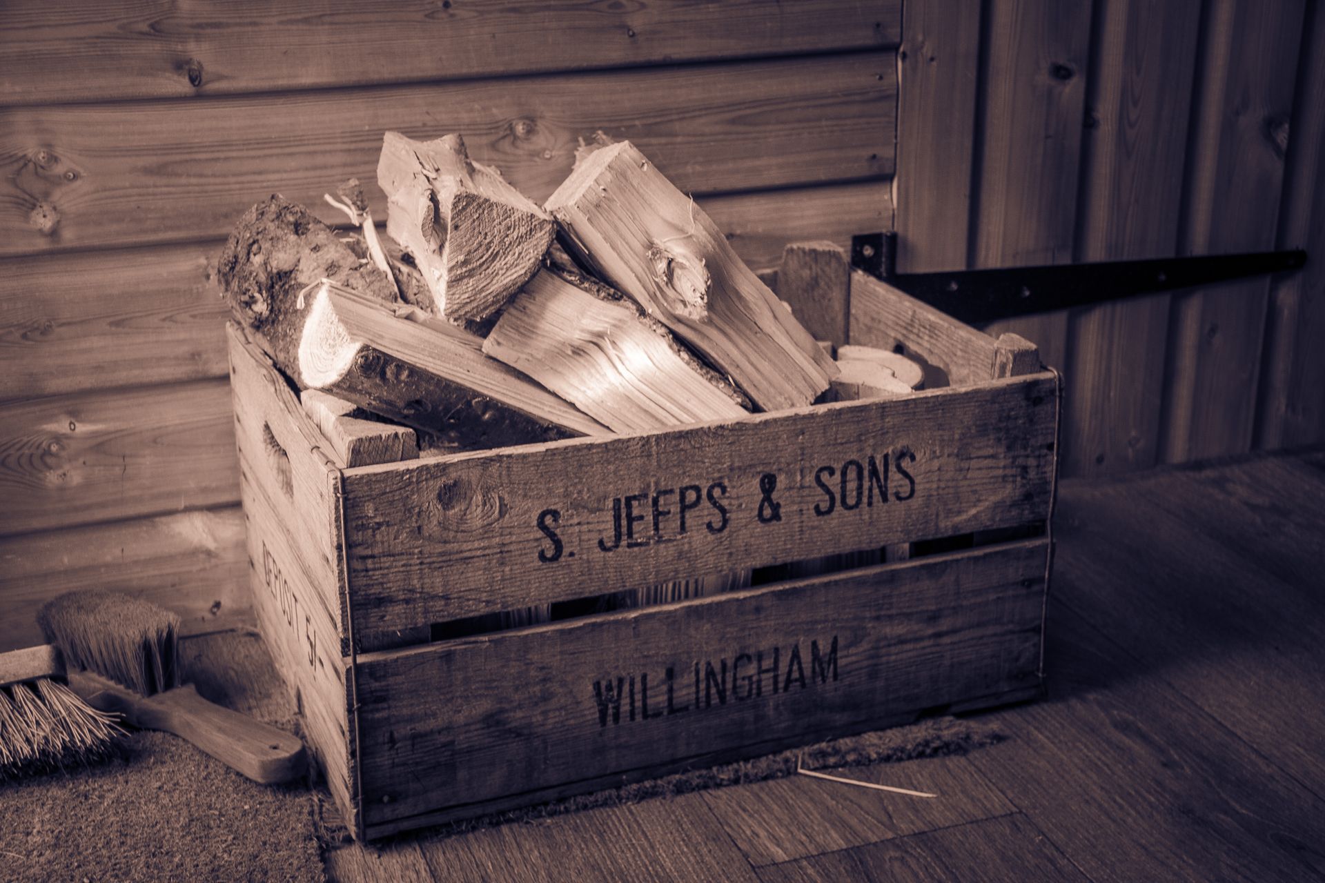 Sepia-toned image of a rustic wooden crate with firewood, capturing a vintage indoor barn setting.