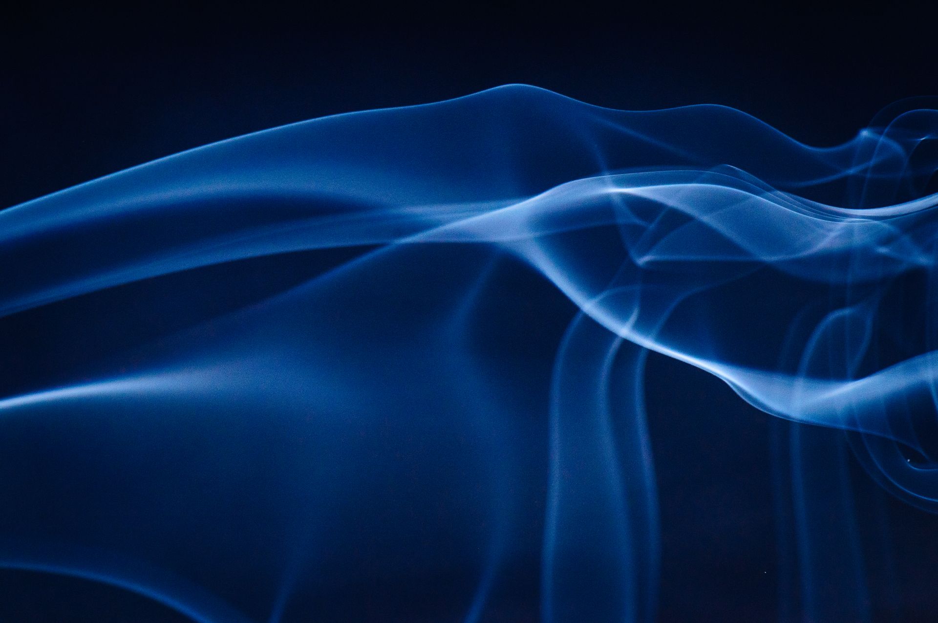 Artistic abstract image of blue smoke on a dark background, creating a mesmerizing wave pattern.