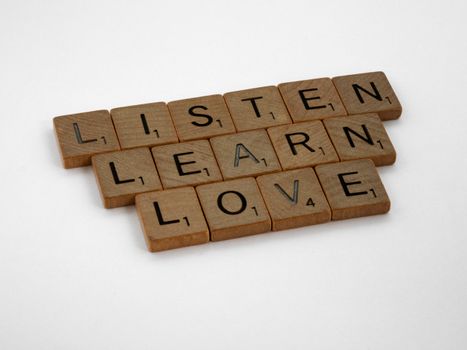 Scrabble tiles arranged to spell Listen, Learn, Love on a white background.