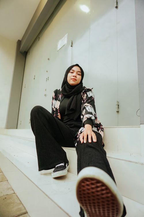 Free Low angle shot of woman in hijab sitting on stairs outdoors in Cirebon, Indonesia. Stock Photo