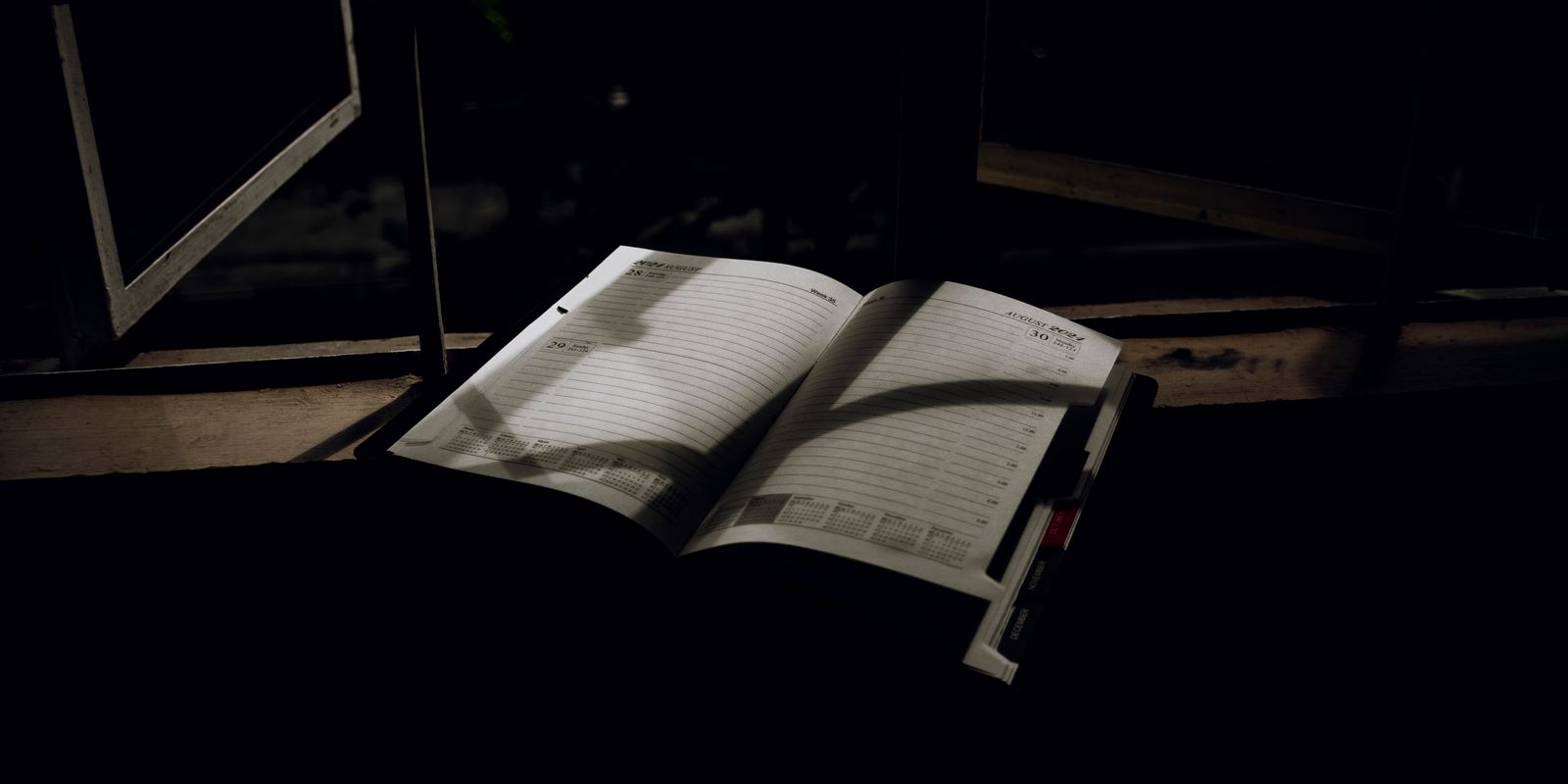 An open planner with dramatic lighting sits on a window sill at night. Ideal for creative projects.