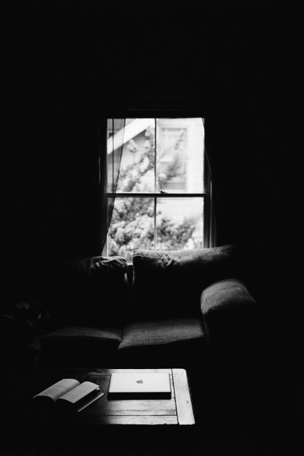 A monochrome living room scene with a couch, book, and laptop by the window.