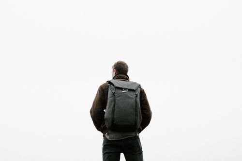 Free A man with a backpack standing outdoors against a vast white sky, evocative of freedom and exploration. Stock Photo