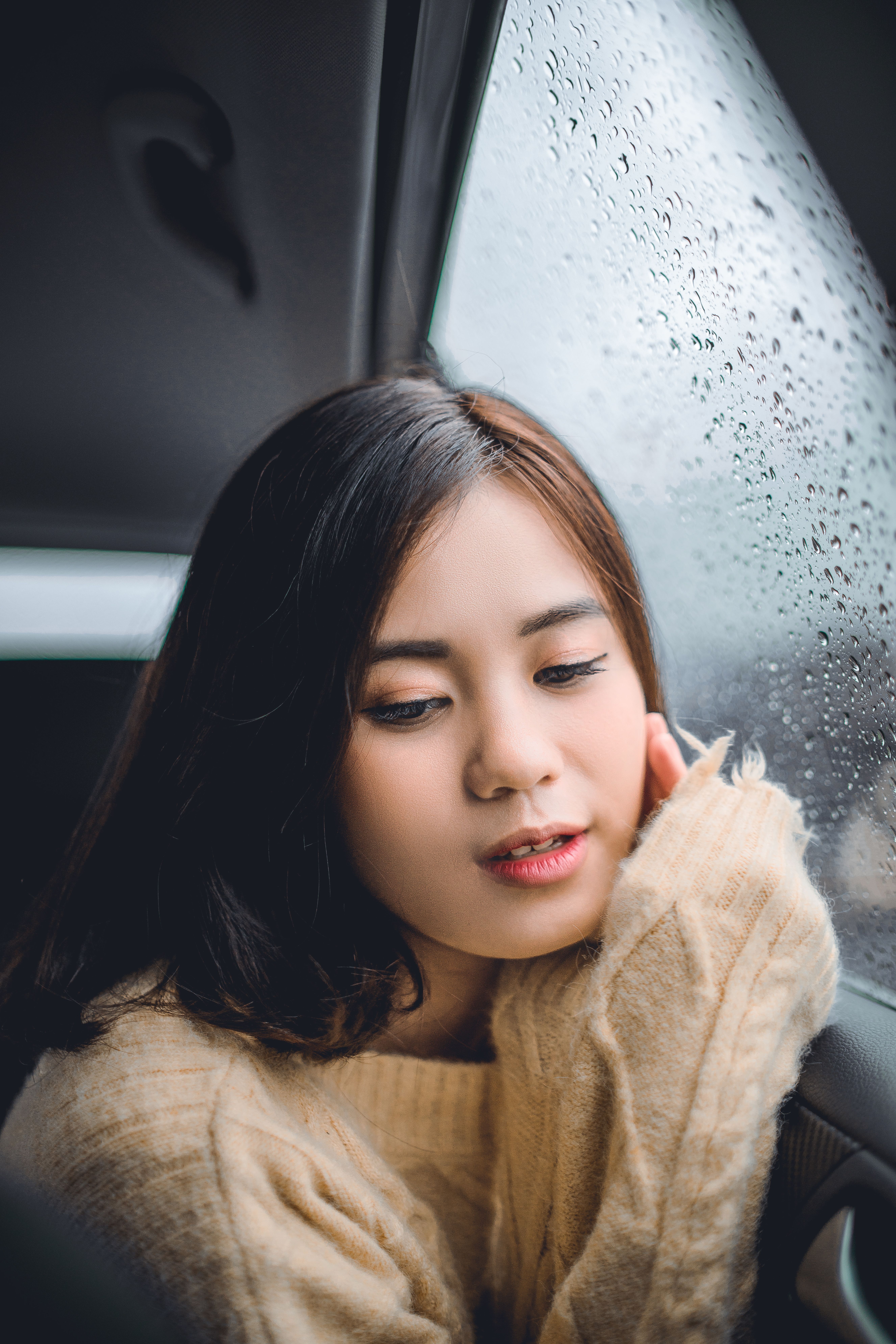 Portrait of a woman in a cozy sweater leaning by a car window on a rainy day.