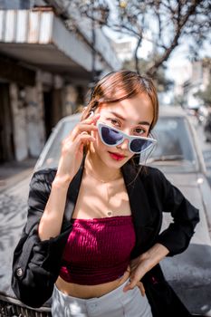 Stylish woman in sunglasses and crop top posing confidently outdoors with old car background.