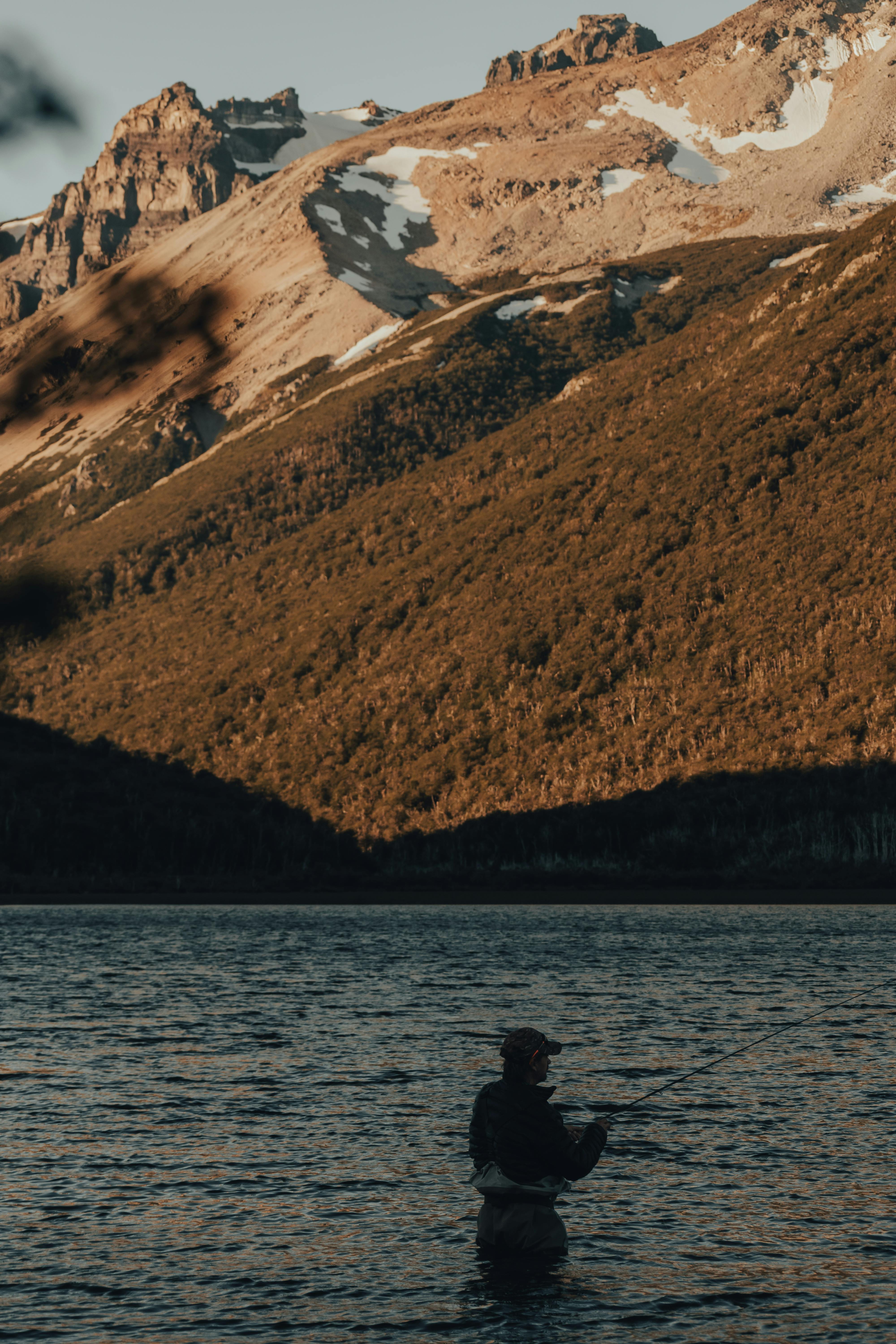 Serene scene of a lone fisherman fly fishing in a mountain lake under the golden evening light.