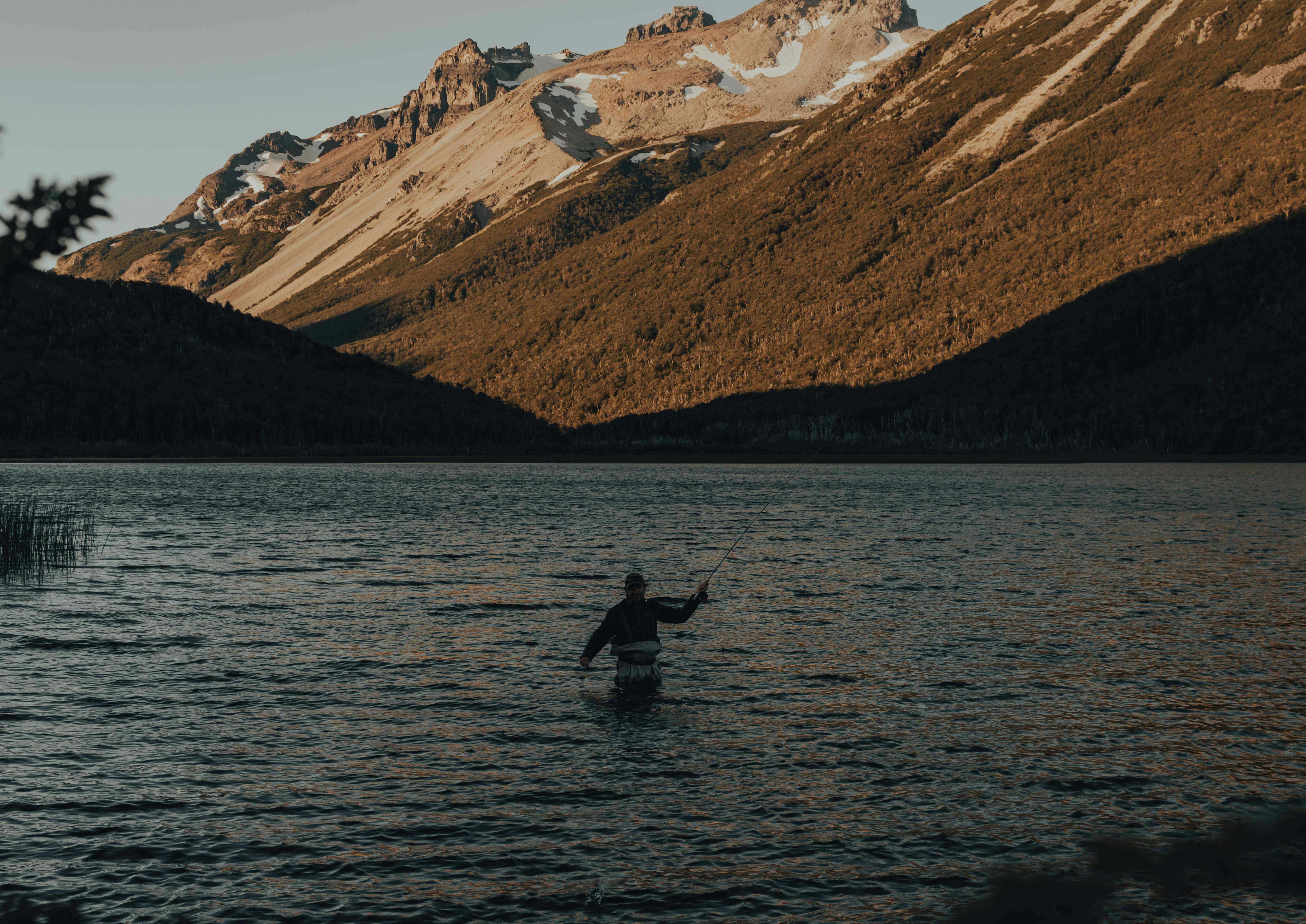 A person fly fishing in a scenic mountain lake during sunset, perfect for leisure and outdoor enthusiasts.