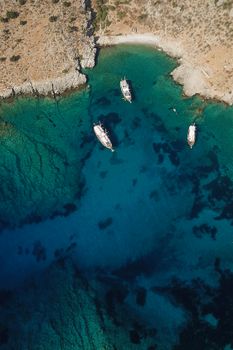 Stunning aerial view of boats anchored in clear turquoise waters along a rocky coastline.