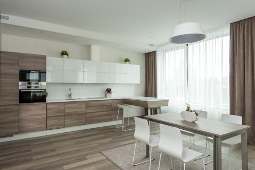Interior of modern kitchen with wooden and white glossy cabinets and dining table with chairs in spacious apartment