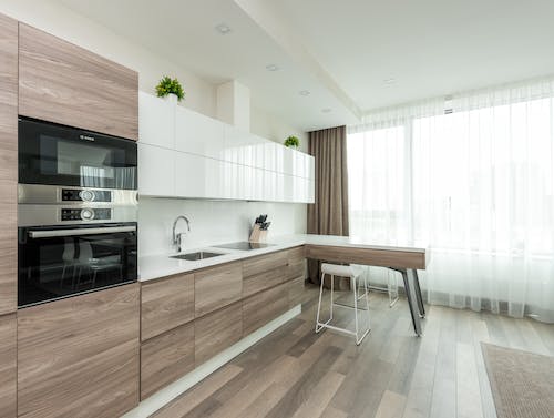 Interior of modern light kitchen with white and wooden cabinets and contemporary appliances in apartment