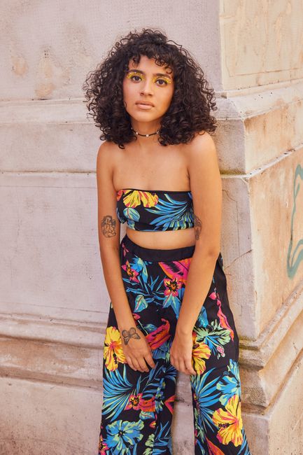 Curly-haired woman posing in vibrant floral outfit against urban architecture.