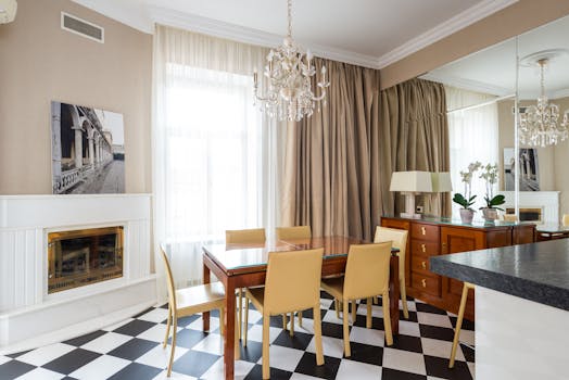 Dining table with chairs placed near window covered with curtains in kitchen with classic chandelier in apartment